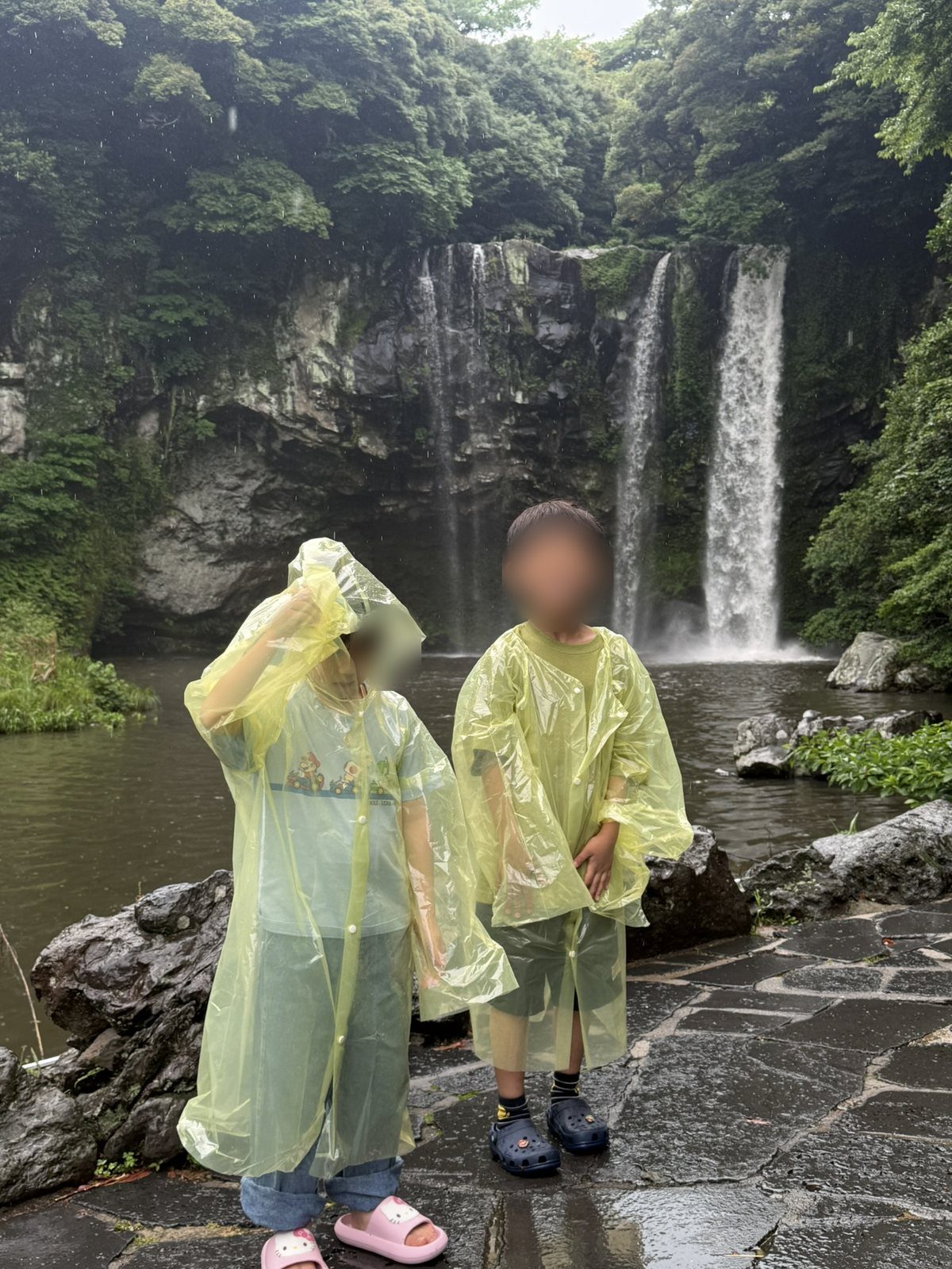 비 오는 날 우비를 입고 천지연폭포 앞에 선 아이들
