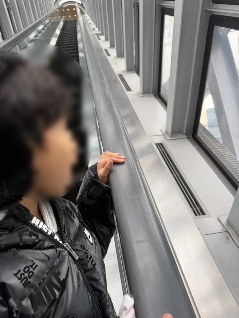 공중 에스컬레이터에서 창밖을 바라보는 아이 사진